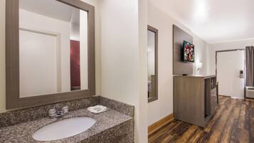 Un baño de hotel con lavamanos de encimera de granito, un espejo y un televisor montado en la pared.
