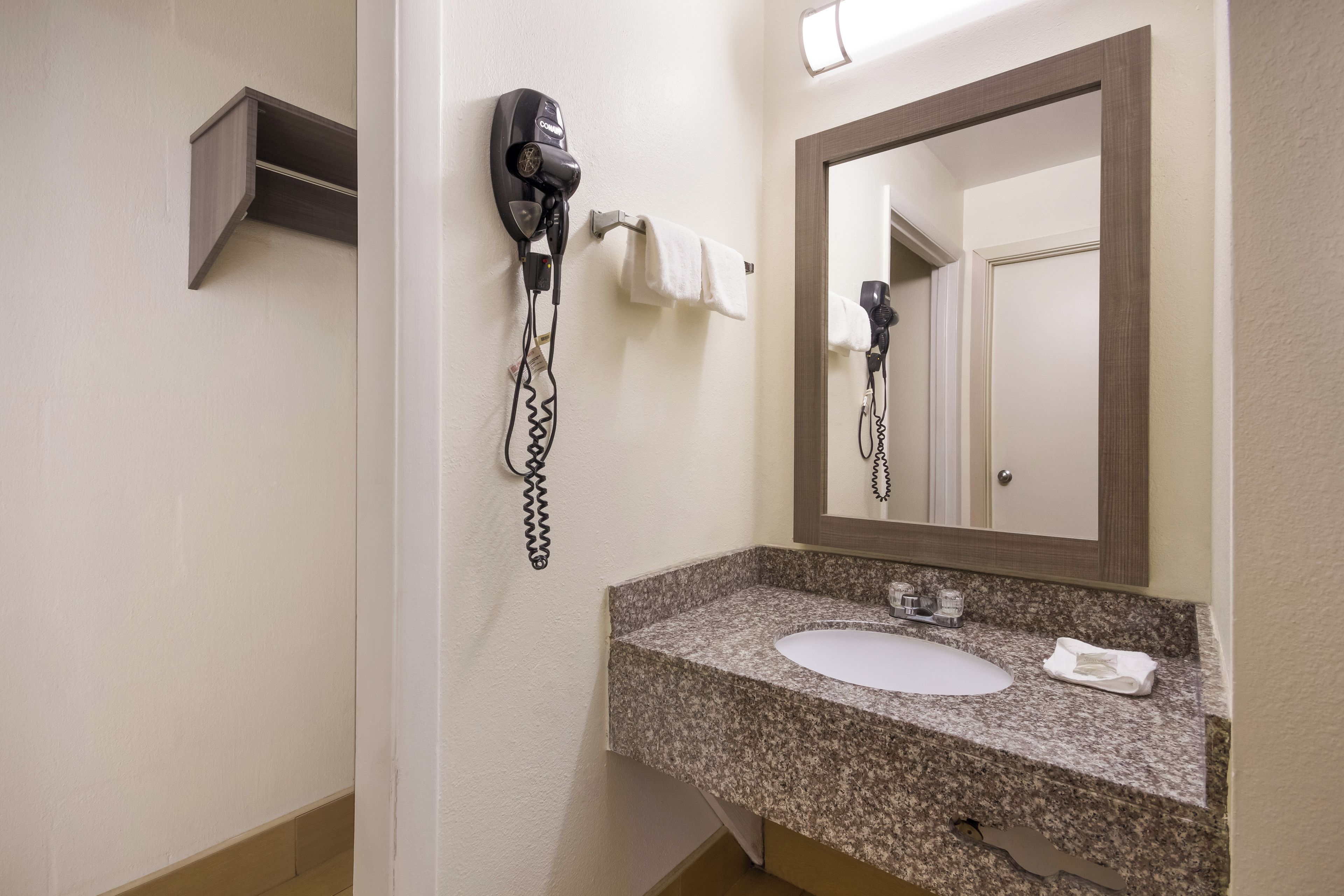 A bathroom with a granite countertop, a sink, a mirror, and two hair dryers mounted on the wall.