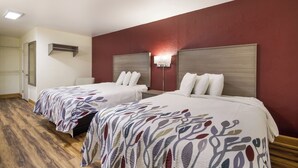 Hotellihuone, jossa on kaksi sänkyä, puulattia, punainen tehosteseinä ja kattovalaisin.