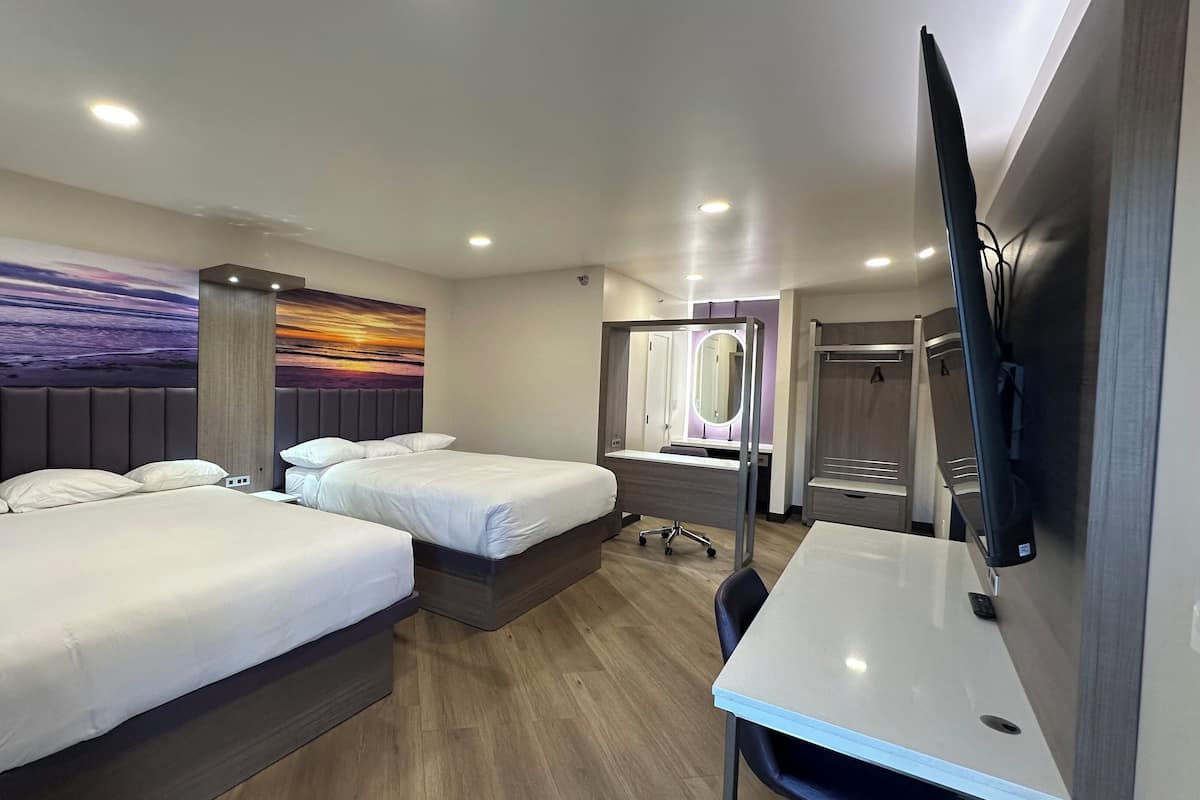 A hotel room with two beds, a desk, a TV, a mirror, and a large wall painting.