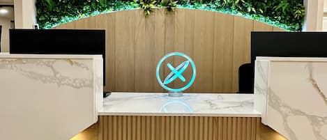 En receptionsdisk med en neonreklame, en væg af træpaneler og en væg med grønne planter.