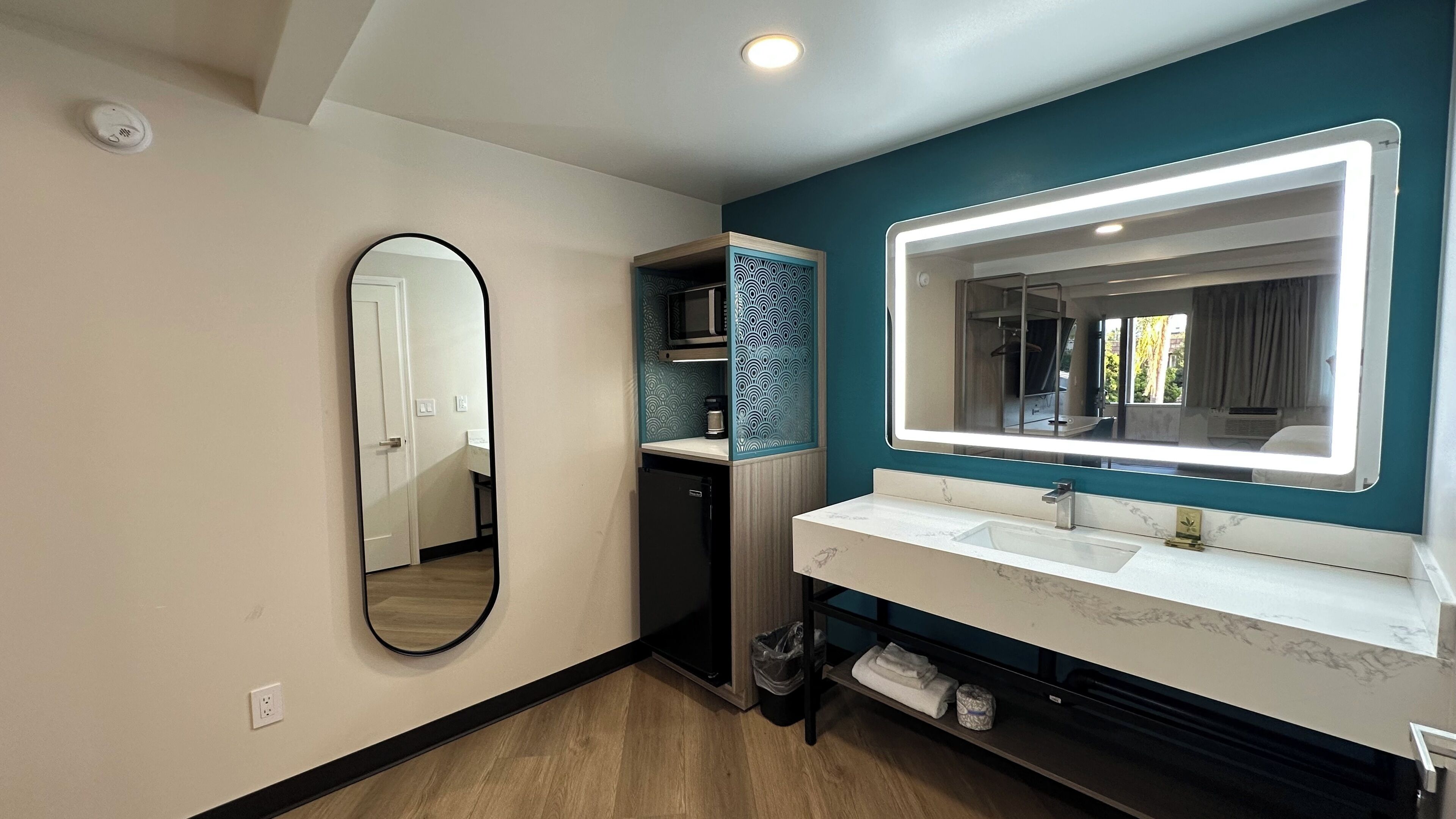 A modern bathroom with a large mirror, two sinks, a shower, and a small storage area.