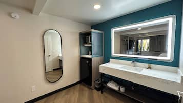 A modern bathroom with a large mirror, two sinks, a shower, and a small storage area.