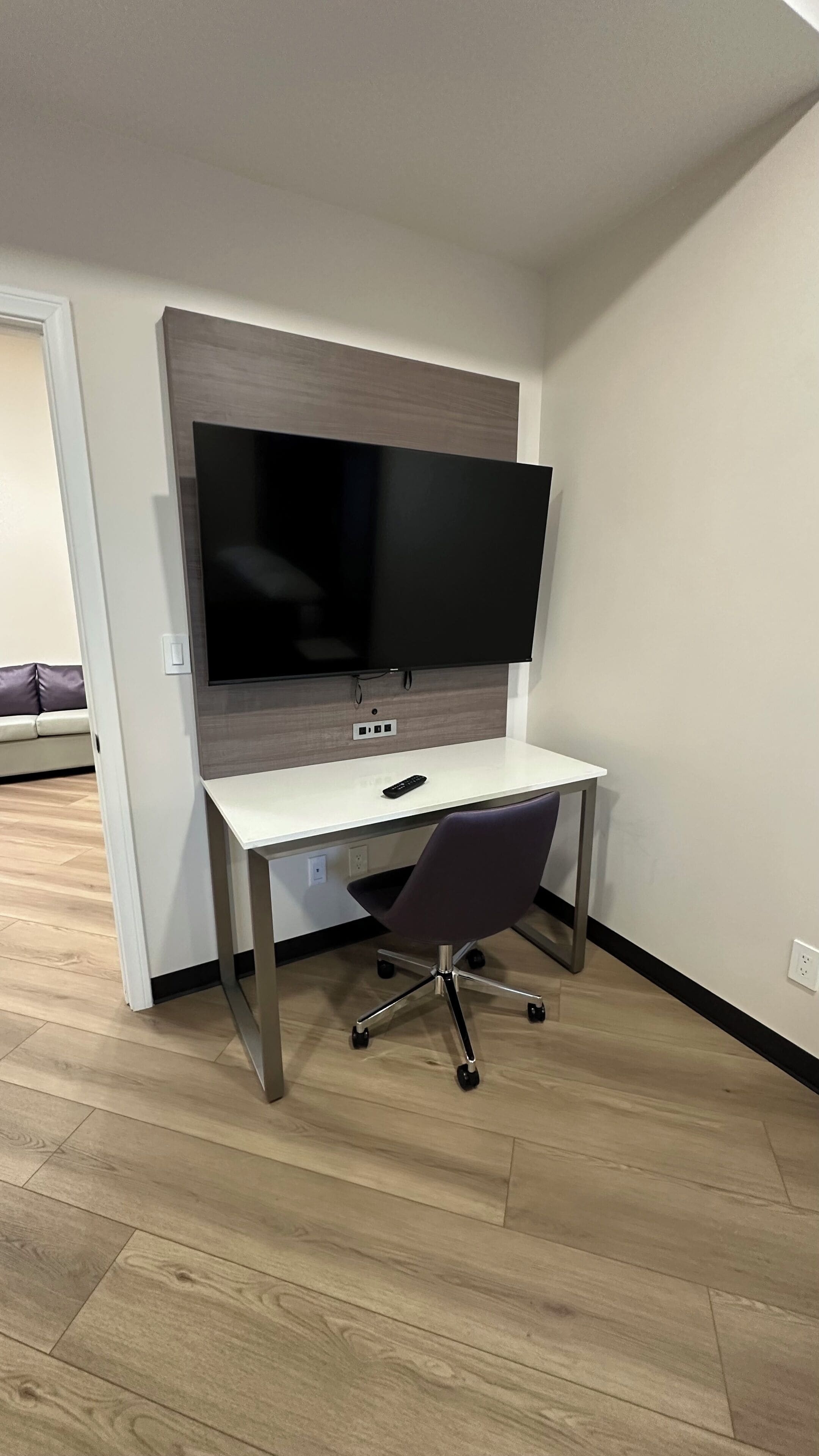 Un espace de bureau moderne avec un bureau blanc, une chaise de bureau noire et un grand téléviseur à écran plat fixé sur un mur en panneaux de bois.