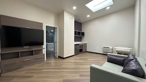 A modern living room with a flat-screen TV, a sofa, and a dining area with a table and chairs.