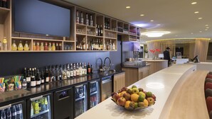 A bar area with shelves of liquor bottles, a refrigerator with drinks, and a fruit bowl on the counter. - Novotel Paris Nord Expo Aulnay Hotel (Aulnay-sous-Bois)
