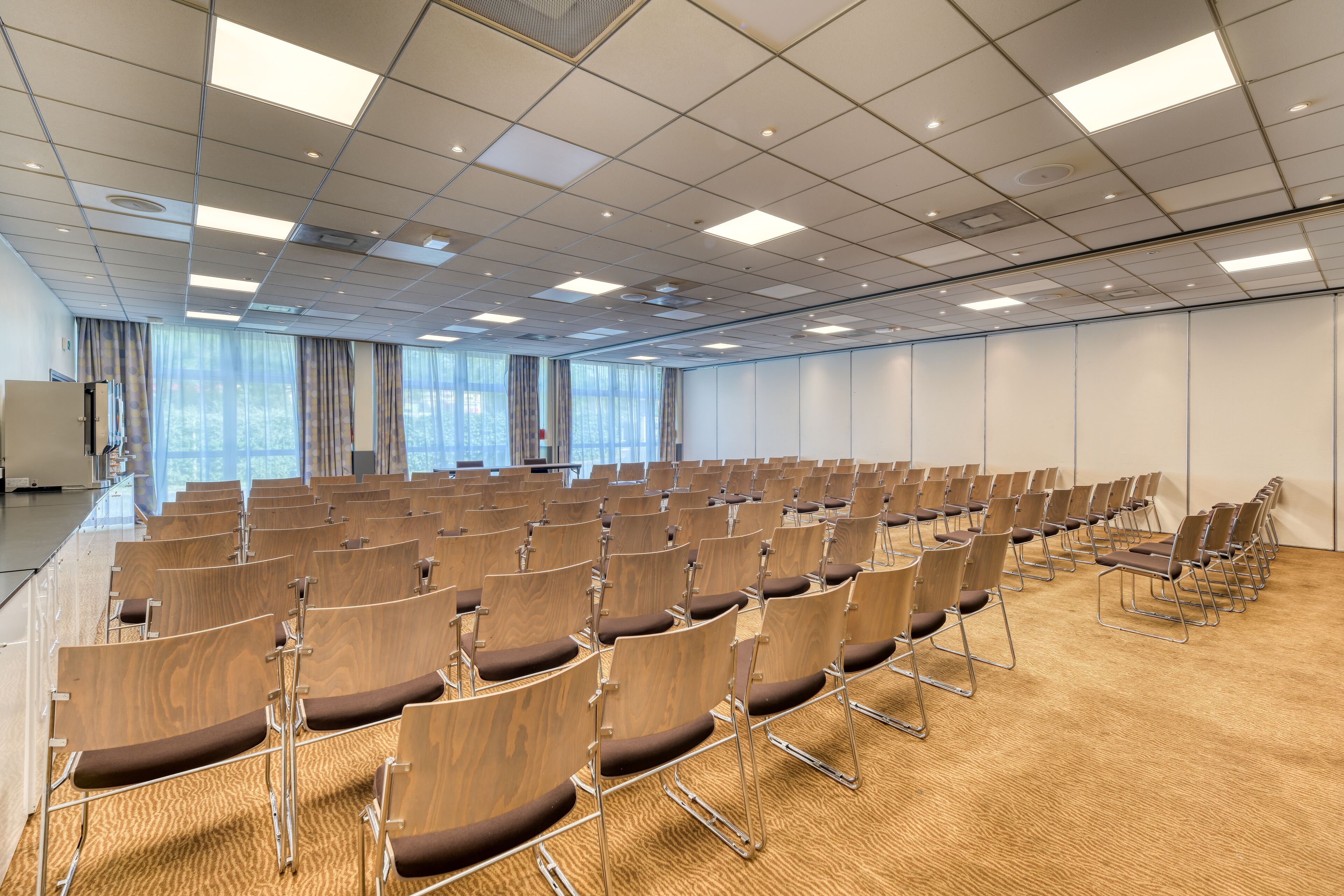 A conference room with rows of chairs, a carpeted floor, and a ceiling with recessed lighting.