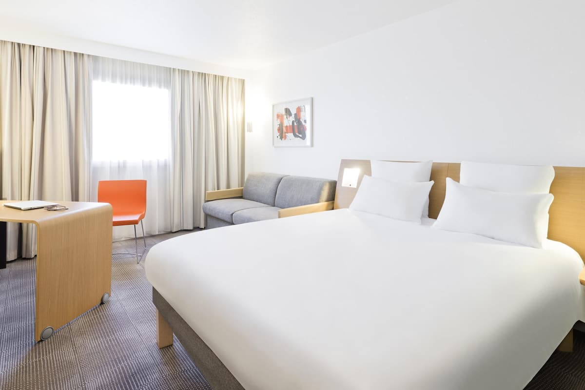 A hotel room with a large bed, a desk, a chair, and a sofa.