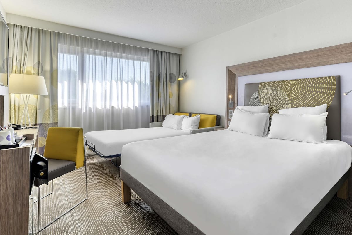 A hotel room with two beds, a desk, a chair, and a large window with curtains.