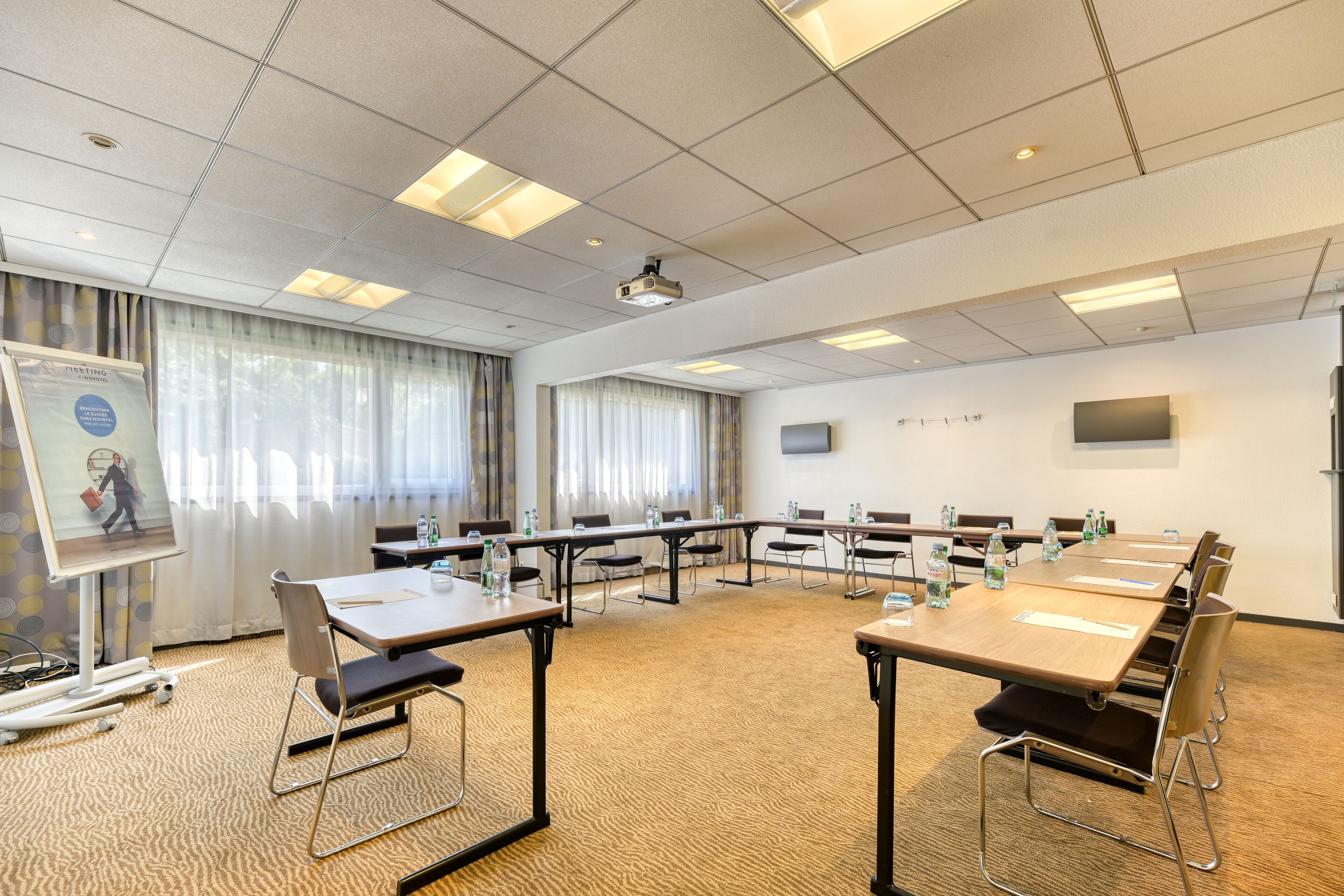 Ein Konferenzraum mit mehreren Tischen, Stühlen und einer Projektionsleinwand.
