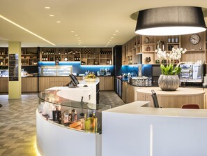 A modern bar area with a glass counter, a Nespresso machine, and a variety of bottles and glasses. - Novotel Paris Nord Expo Aulnay Hotel (Aulnay-sous-Bois)