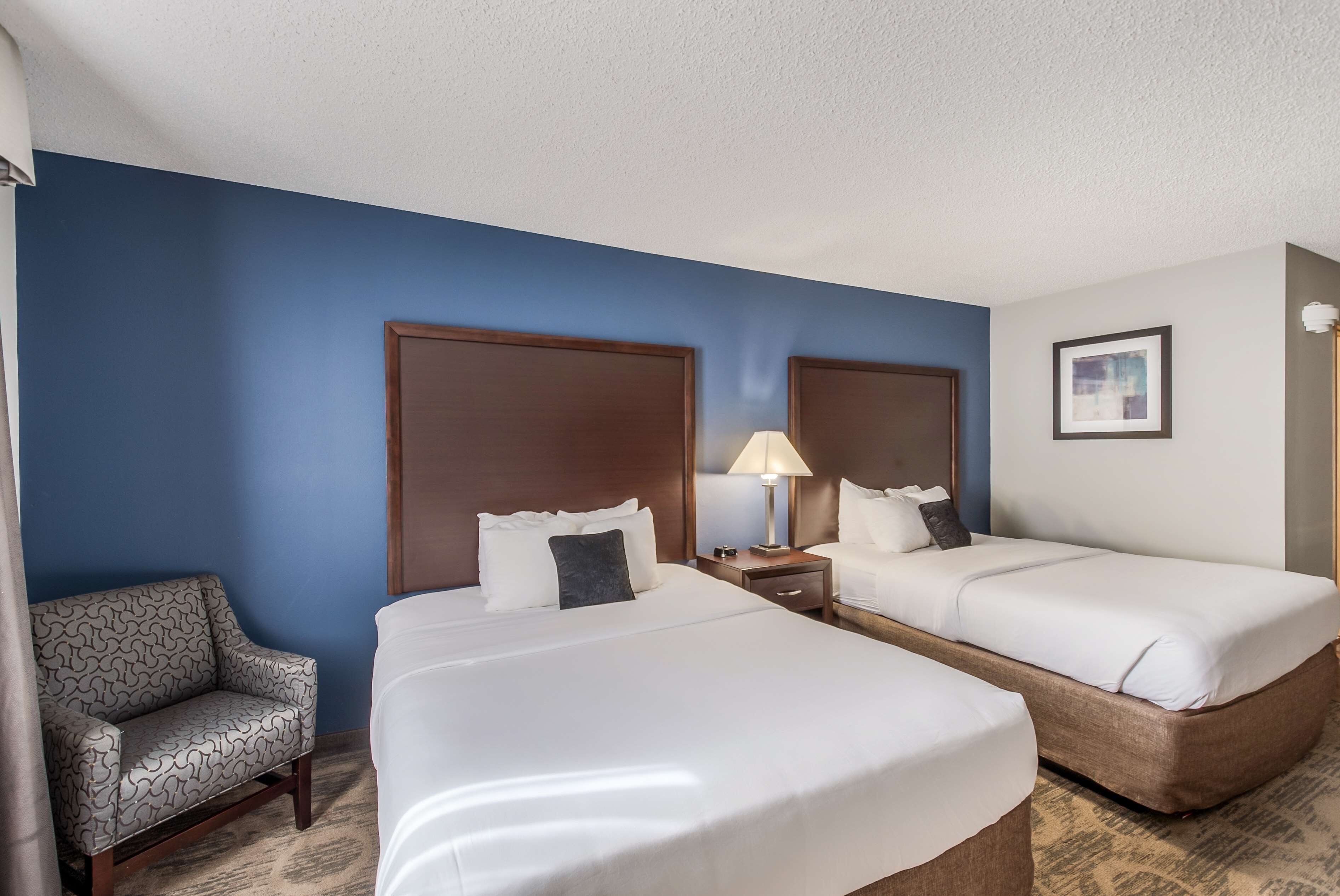 A hotel room with two single beds, a sofa, a nightstand with a lamp, and a framed picture on the wall.