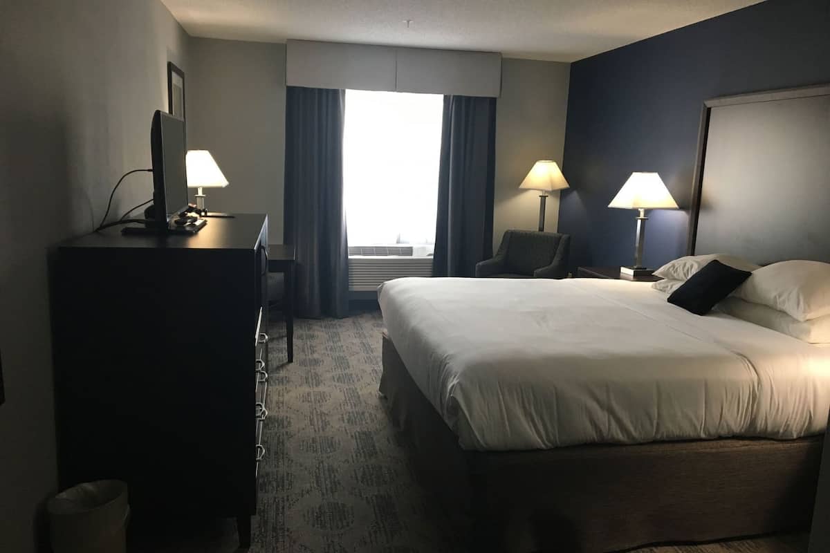 Une chambre d’hôtel équipée d’un lit, d’un bureau, d’une chaise, de lampes et d’une fenêtre avec des rideaux.