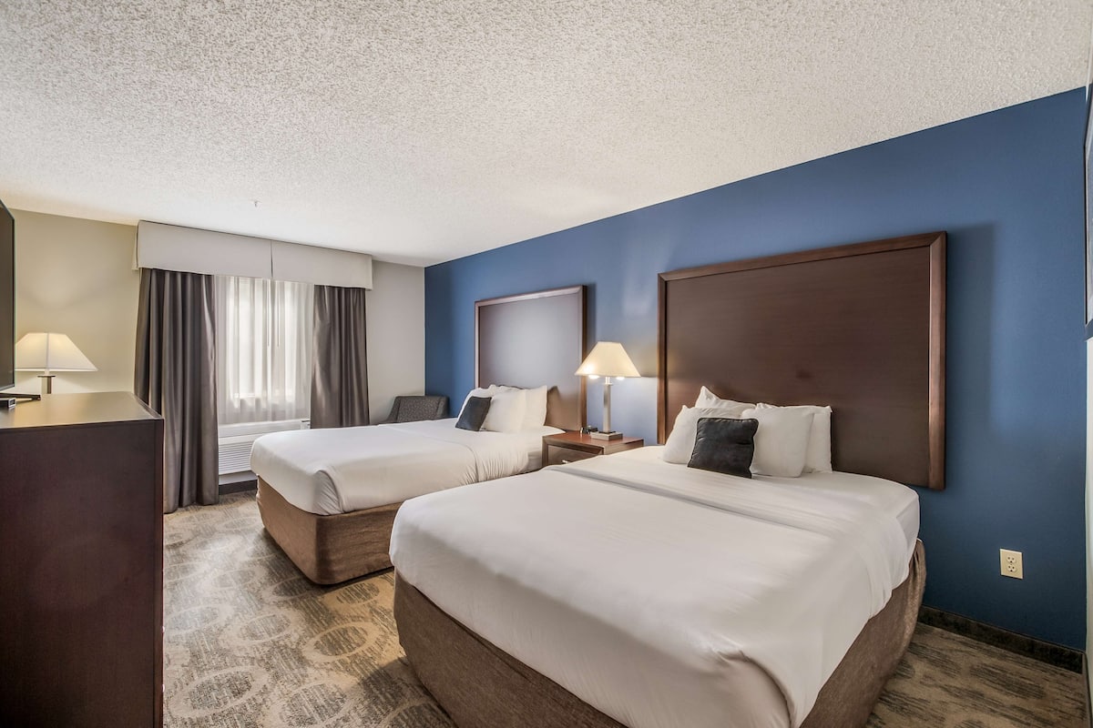 Une chambre d’hôtel avec deux lits, un bureau et une grande fenêtre avec des rideaux.
