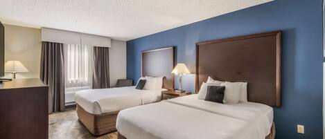 A hotel room with two beds, a desk, and a large window with curtains.