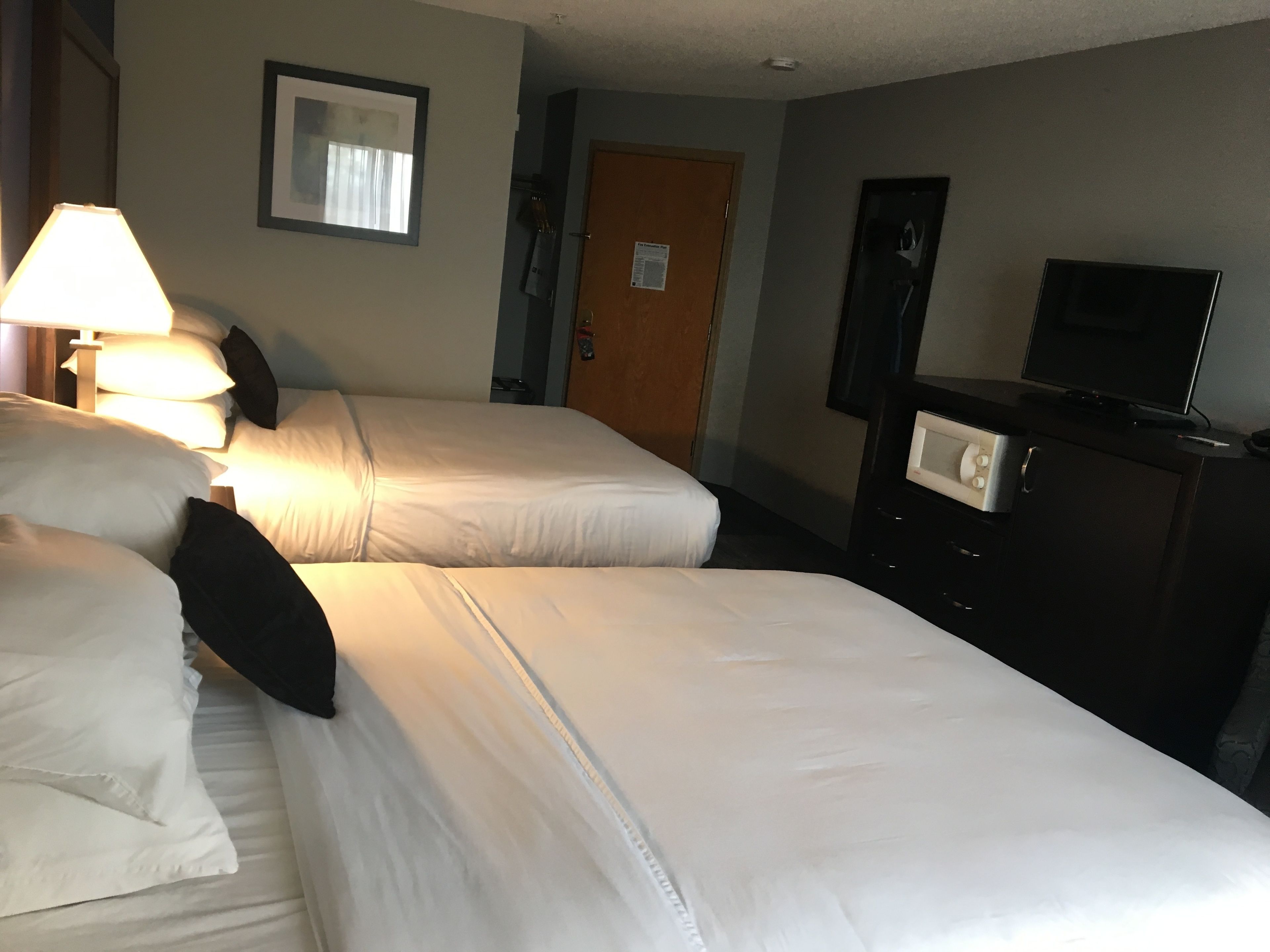 Ein Hotelzimmer mit zwei Betten, einem Fernseher, einer Kommode und einer Lampe.