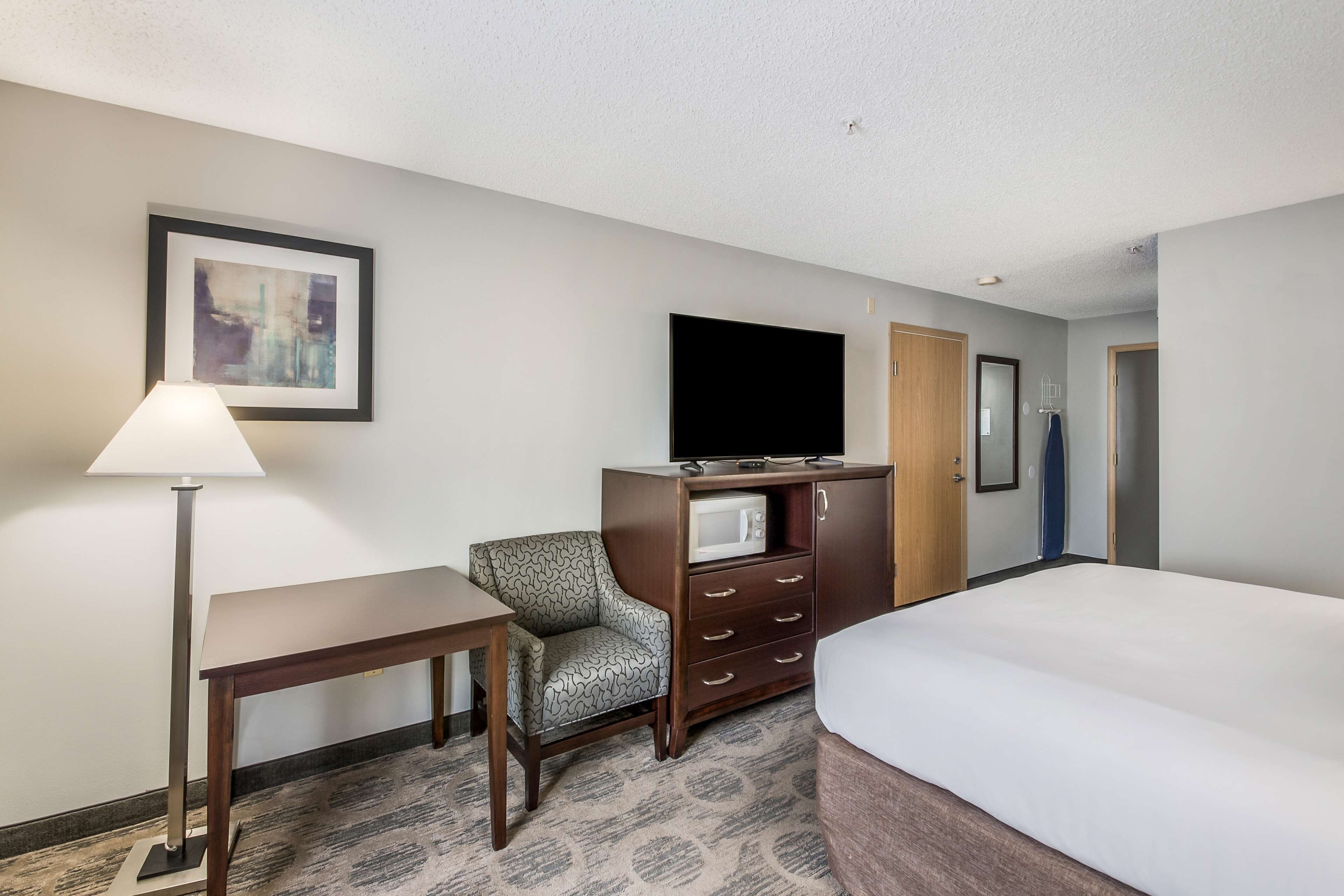 Une chambre d’hôtel équipée d’un lit, d’un bureau, d’une chaise, d’une télévision, d’un four à micro-ondes et d’une porte.