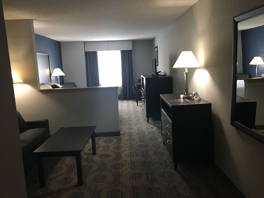 A hotel room with a bed, a desk, a chair, a dresser, a mirror, and a lamp.
