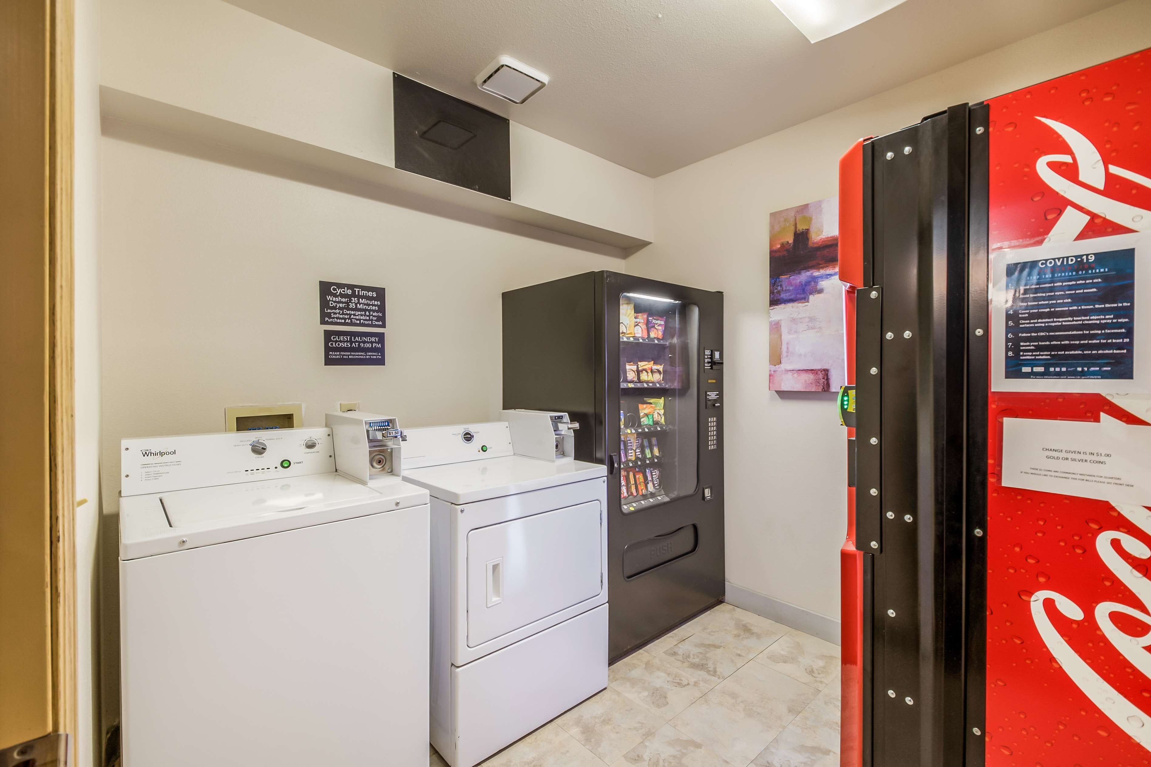 Un área de lavandería con dos lavadoras Whirlpool, una máquina expendedora y un refrigerador Coca-Cola.