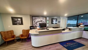 A reception area with a counter, two leather chairs, framed pictures on the wall, and a blue mat with "BAYMONT" text. - Baymont by Wyndham Great Falls City Center (Great Falls)