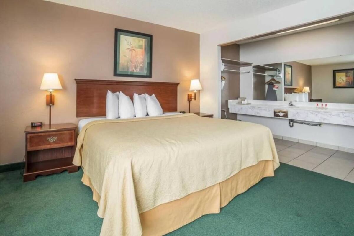 Une chambre d’hôtel comprenant un lit, des lampes de chevet, une table de chevet, un grand miroir et un meuble-lavabo dans la salle de bain.