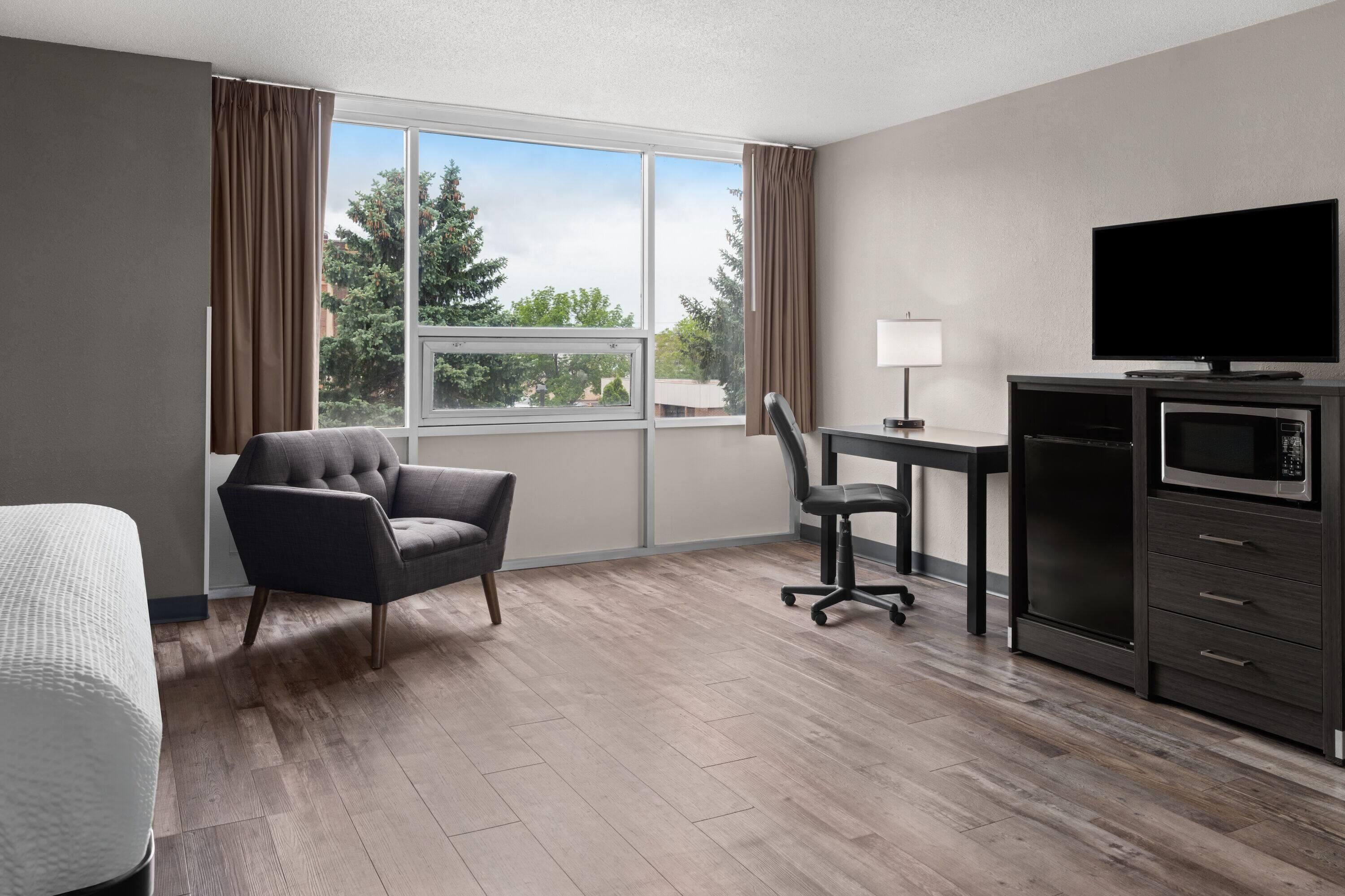 A hotel room with a bed, a desk, a chair, a television, a microwave, and a window with curtains.