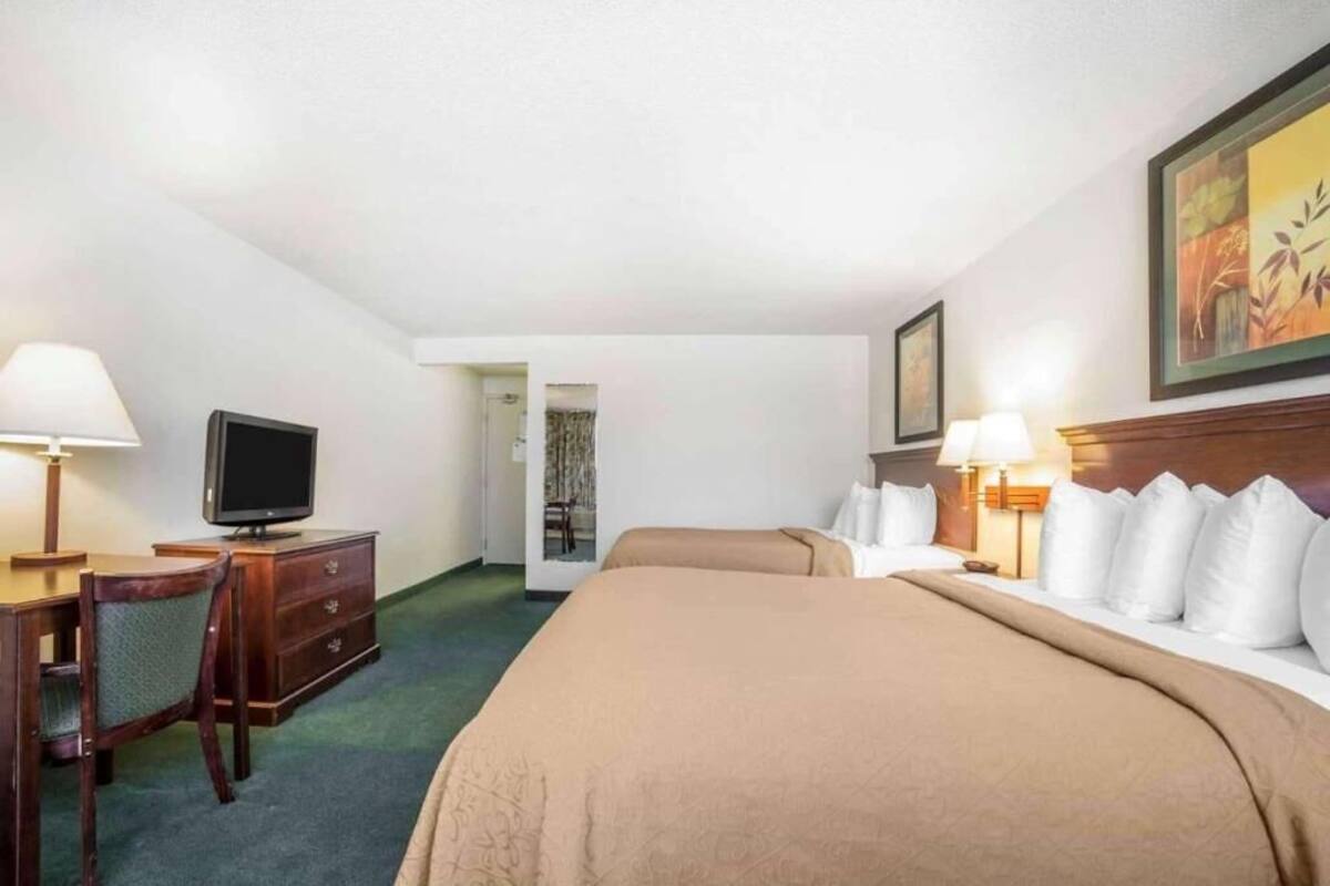 Une chambre d’hôtel avec un lit, un bureau avec une télévision, une chaise, une lampe et un tableau au mur.