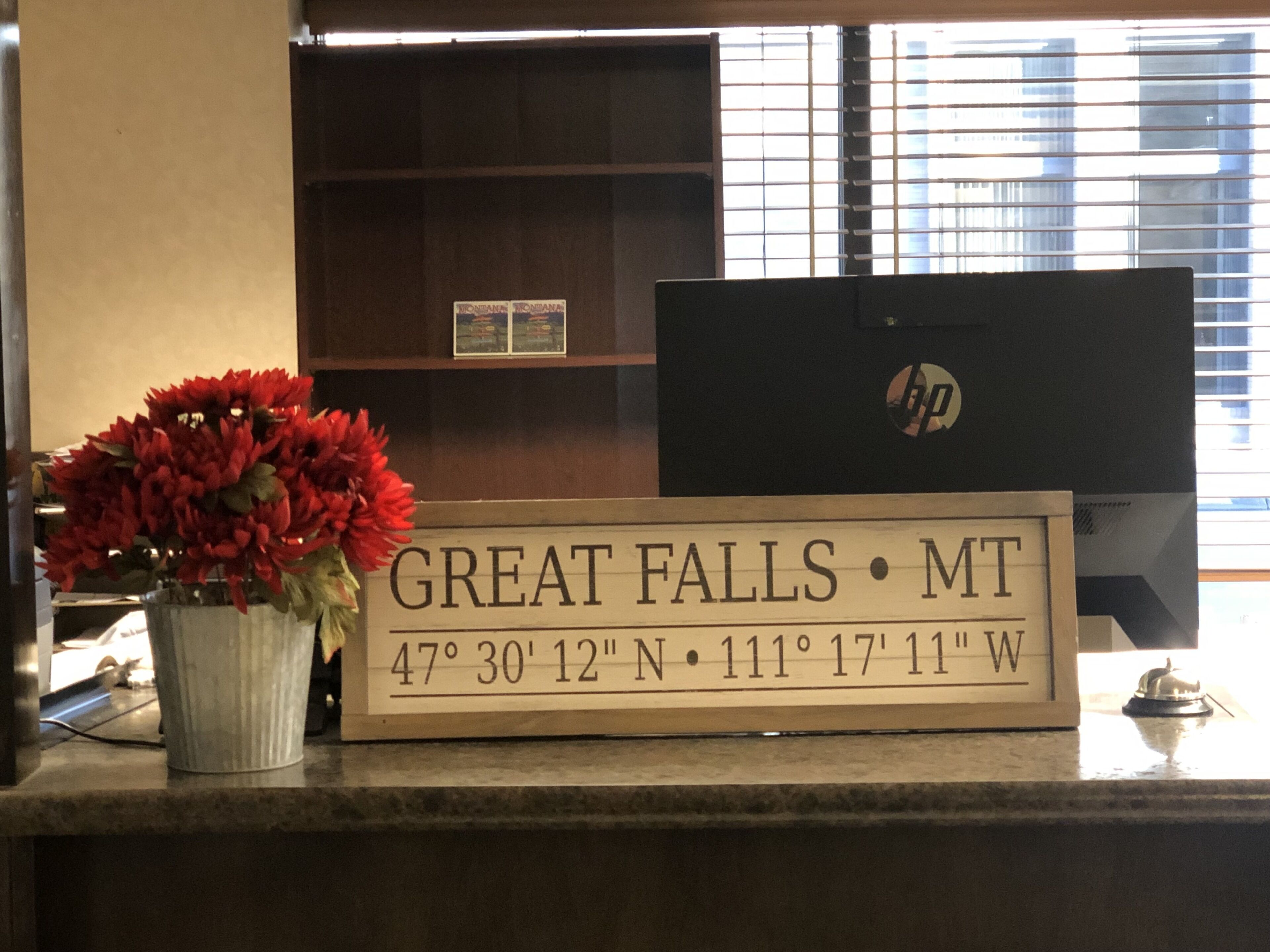 Taulell de recepció amb un senyal que indica la localitat com Great Falls, MT, i coordenades.