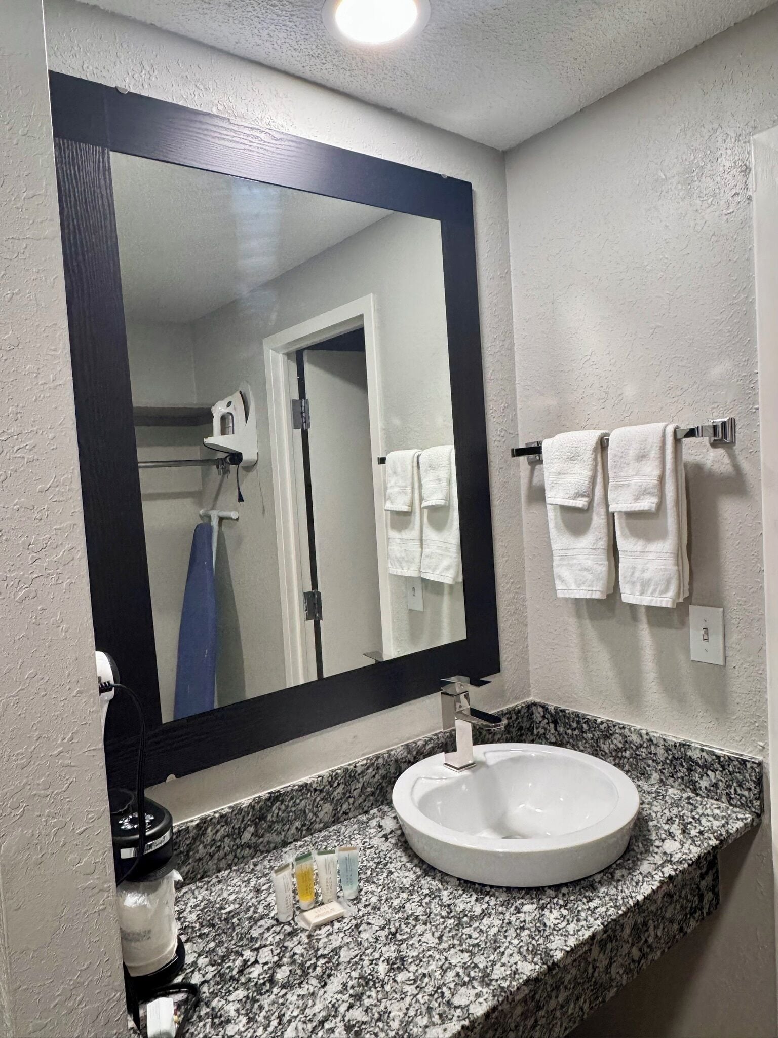 A bathroom with a large mirror, white sink, granite countertop, and two towels hanging on a rack.