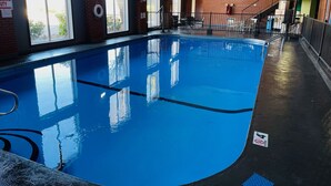 An indoor swimming pool with clear blue water, surrounded by brick walls and large windows.