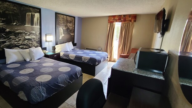 Habitación de hotel con dos camas, un escritorio, una silla, un televisor y un gran cuadro mural que representa cascadas.