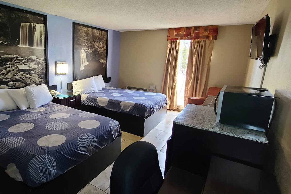 A hotel room with two beds, a desk, a chair, a TV, and large wall art depicting waterfalls.