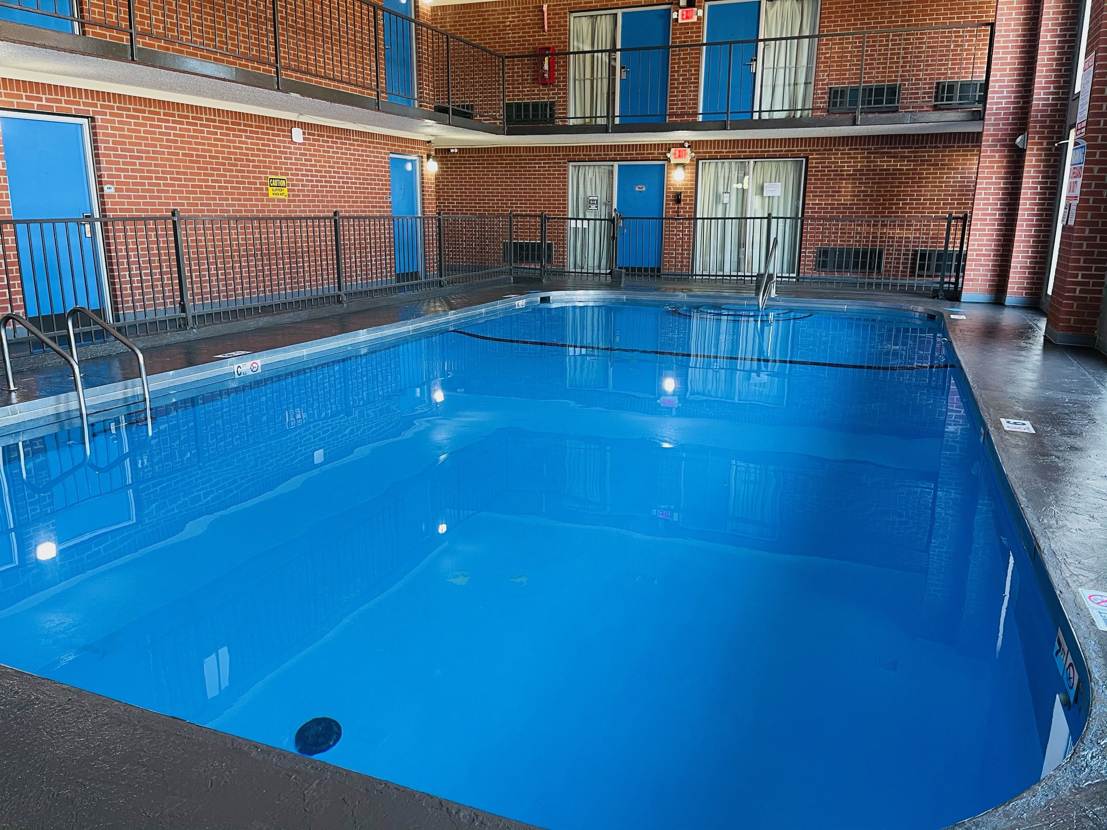 An indoor swimming pool with a clear blue water surface, surrounded by a brick wall with blue doors and windows.