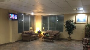 Un hallo amplio con dos sofás, una mesa de centro, un televisor en la pared y ventanas grandes con persianas.