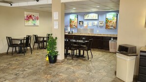 Un restaurante con varias mesas y sillas, una planta en maceta y obras de arte en las paredes.