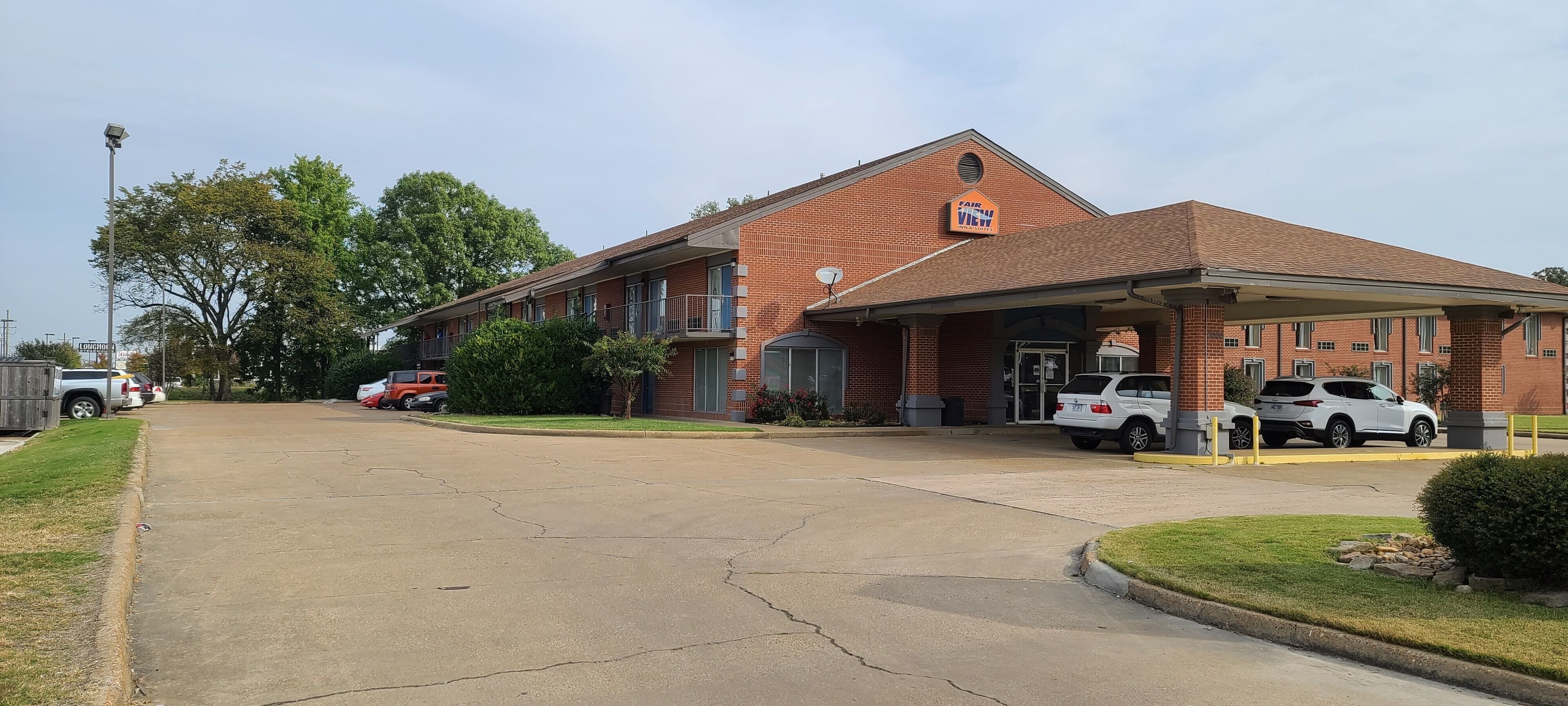 Un motel en briques doté d’un parking couvert, où plusieurs voitures sont stationnées, et d’une pelouse à l’avant.