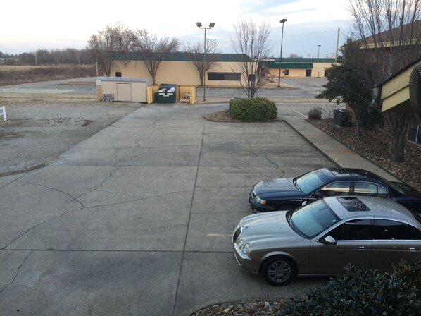 A parking lot with two cars parked, a building with a green roof, and a small shed in the background.