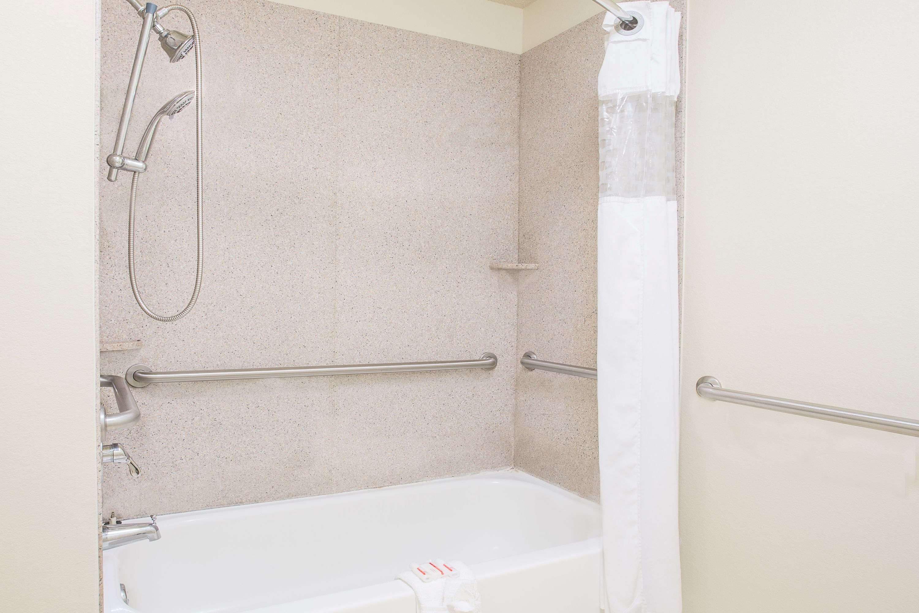 Ein Badezimmer mit einer weißen Badewanne, einer Duschbrause und Haltegriffen.