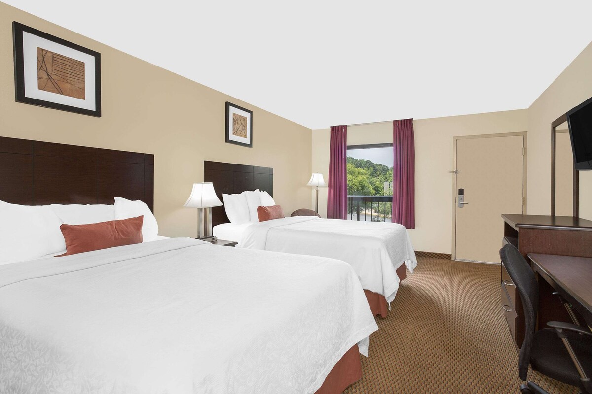 Une chambre d’hôtel avec deux lits, un bureau, une chaise, une télévision et une fenêtre donnant sur un beau paysage.