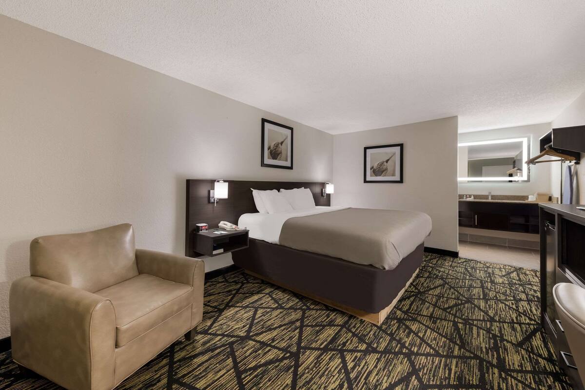 A hotel room with a bed, a chair, a nightstand, a desk, and a television.