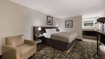 A hotel room with a bed, a chair, a nightstand, a desk, and a television.
