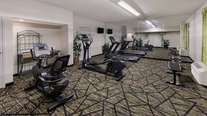 A gym with multiple exercise machines, including treadmills and an elliptical, and a mirrored wall.