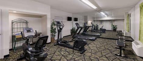 Uma academia com vários equipamentos de exercício, incluindo esteiras e uma elíptica, e um espelho grande na parede.