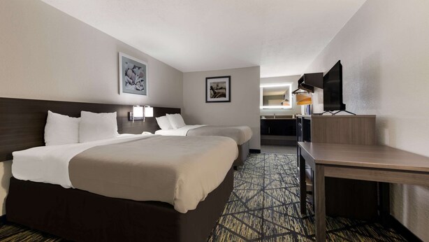 A hotel room with two beds, a desk, a television, and artwork on the walls.