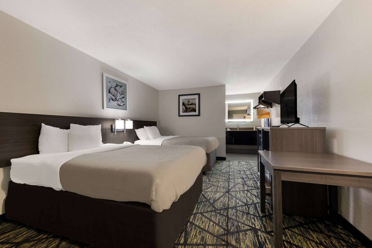 A hotel room with two beds, a desk, a television, and artwork on the walls.