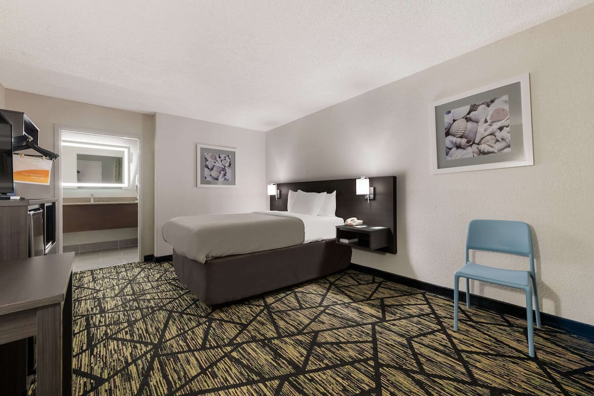 A hotel room with a bed, a desk, a chair, a nightstand, and two wall-mounted lamps.