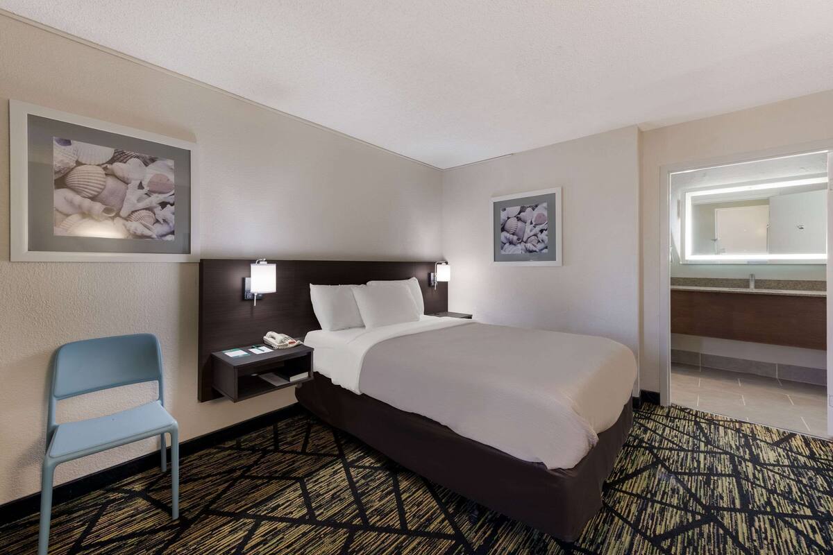 A hotel room with a bed, a nightstand, a chair, and two framed pictures on the wall.