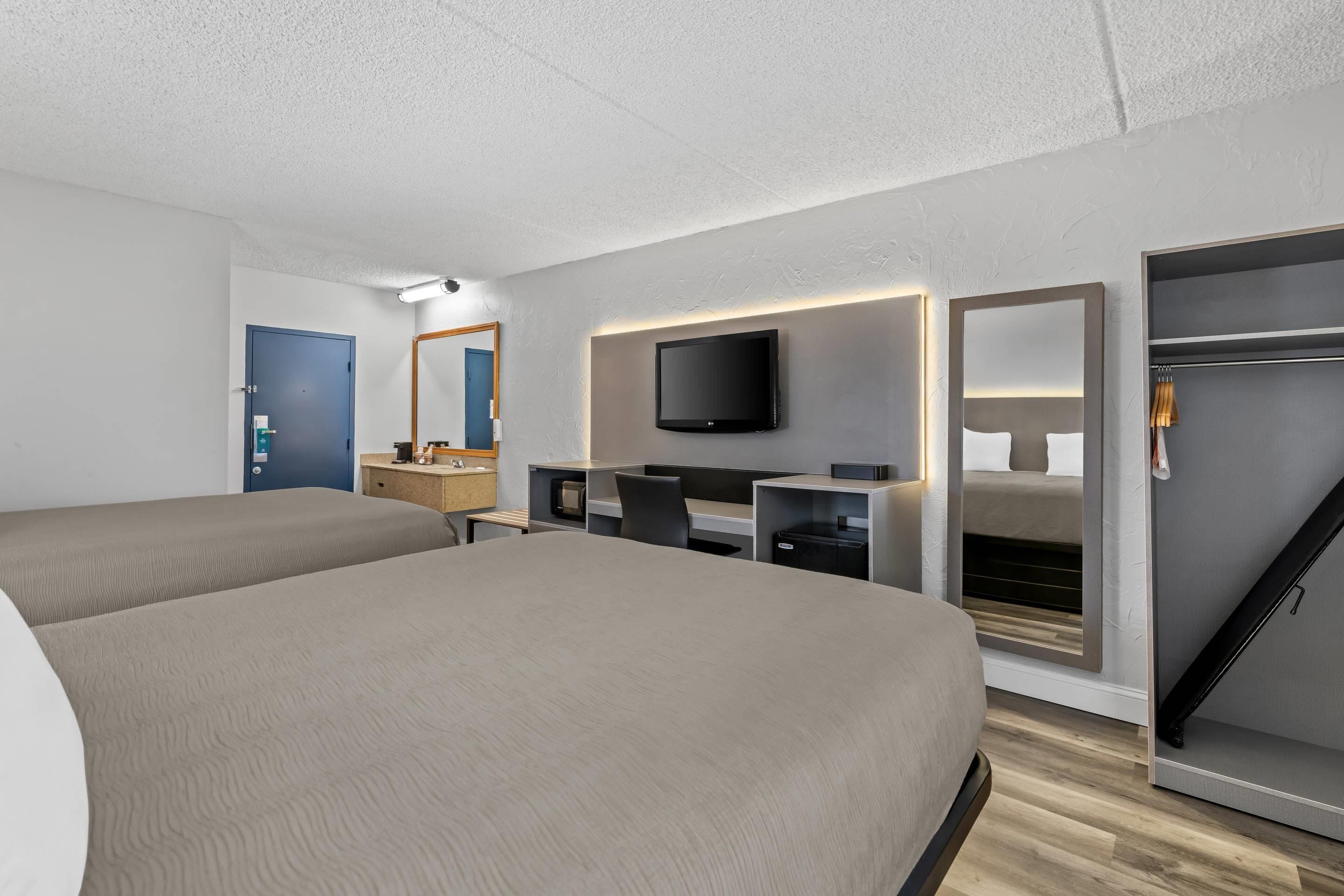Una habitación de hotel moderna con dos camas, un escritorio, un televisor y un armario.