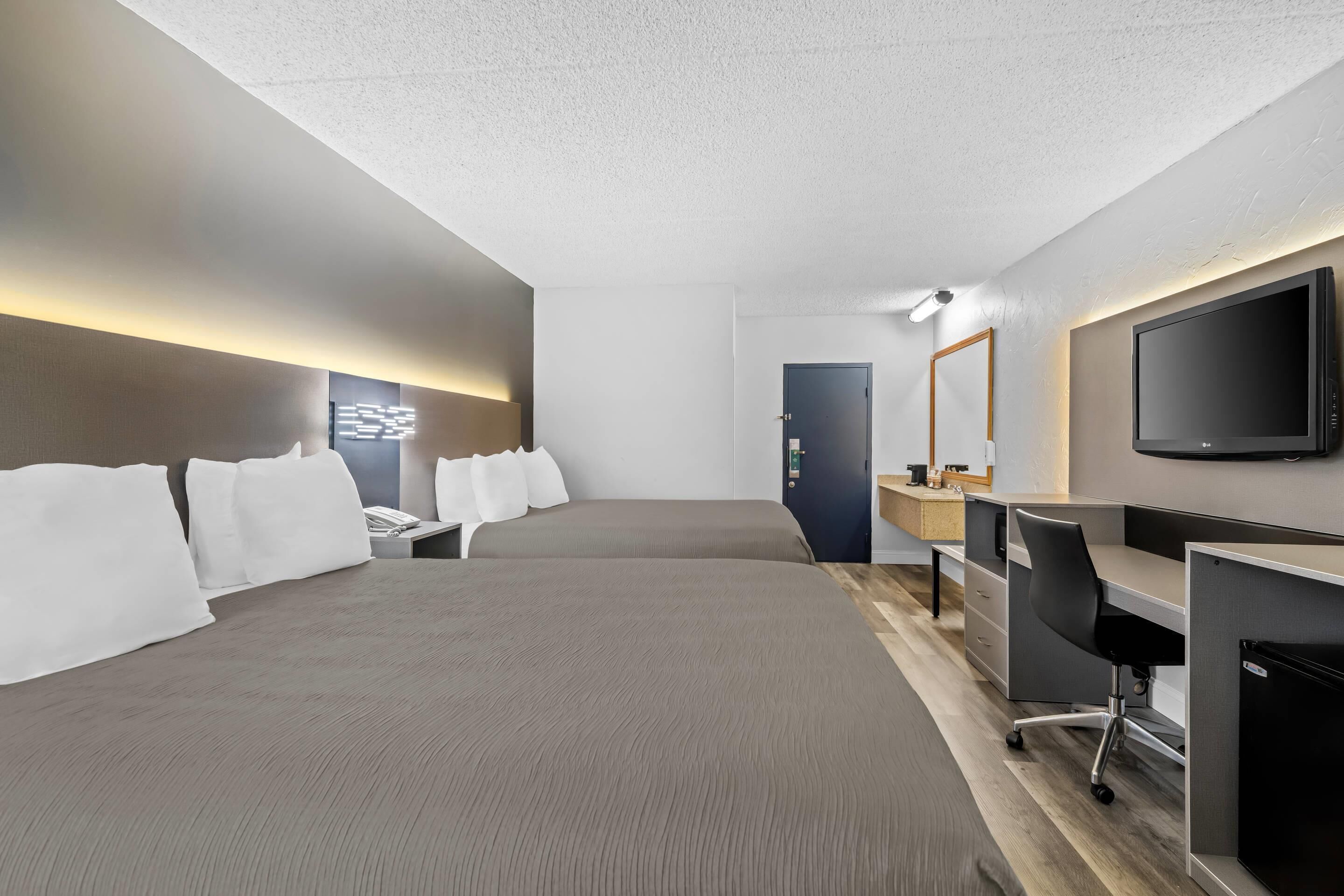 A modern hotel room with a large bed, a desk, a chair, a television, and a door.