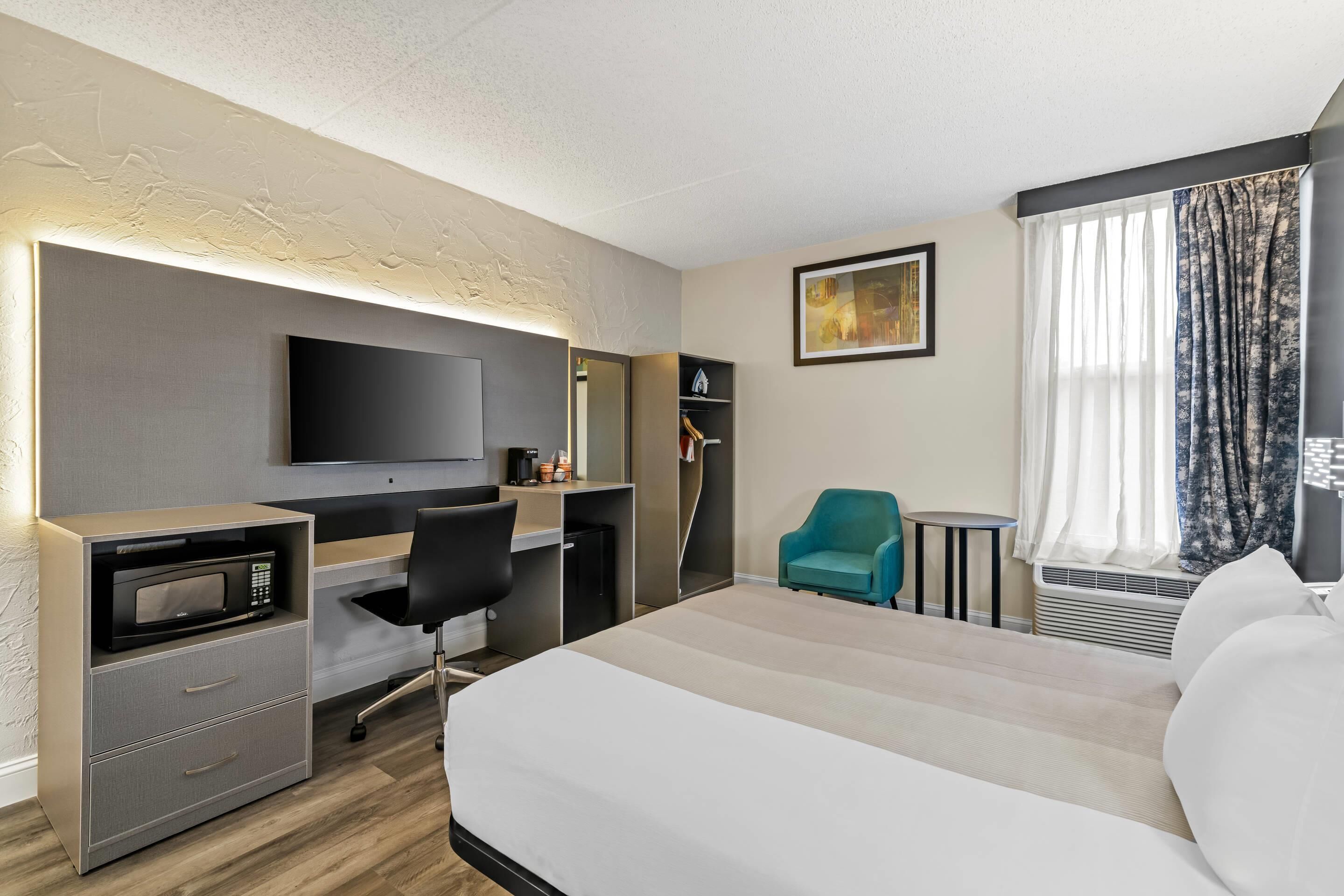 Habitación de hotel con cama, escritorio con computadora, microondas, silla, televisión y ventana con cortinas.
